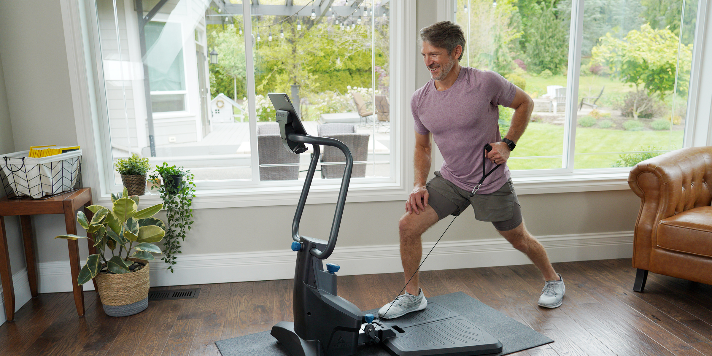 A man in athletic wear uses a FitForm home Gym in a bright living room with large windows.